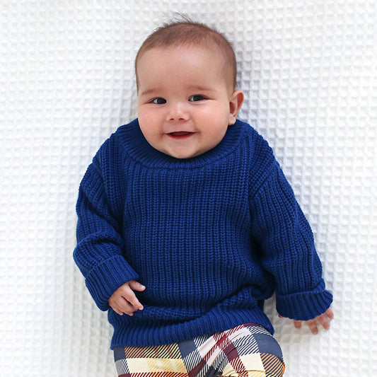 Baby wearing a blue sweater and plaid pants on a white blanket